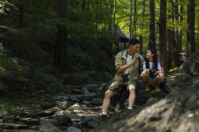 父亲和女儿坐在杉树森林中的石头上、吹着小电风扇休息图片下载