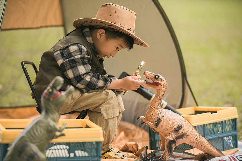 男孩在户外帐篷里玩恐龙玩具图片下载