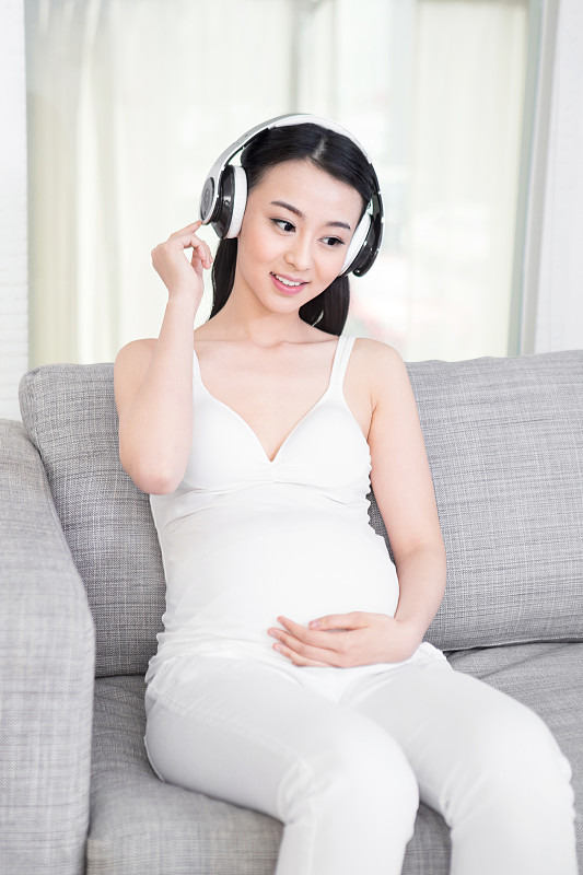 坐在沙发上戴耳机的孕妇图片素材