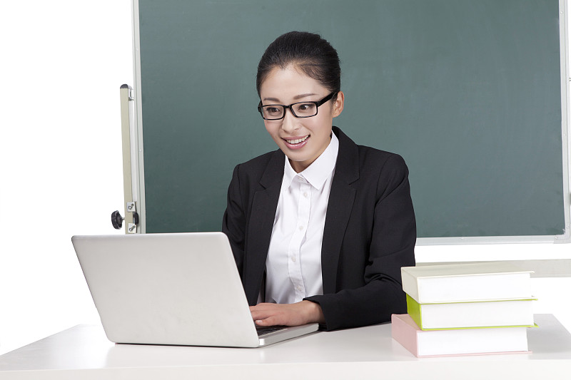 一个青年女教师坐在黑板前使用电脑备课图片下载