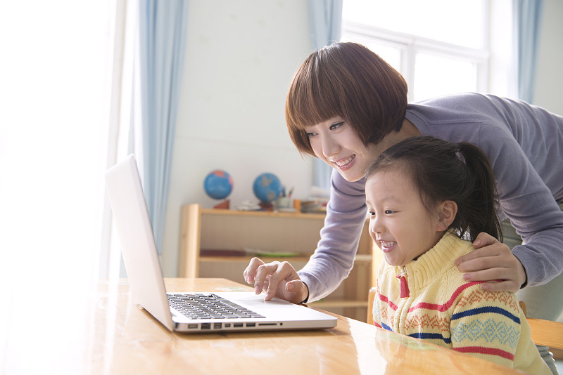Kindergarten teacher and girl using laptop图片下载