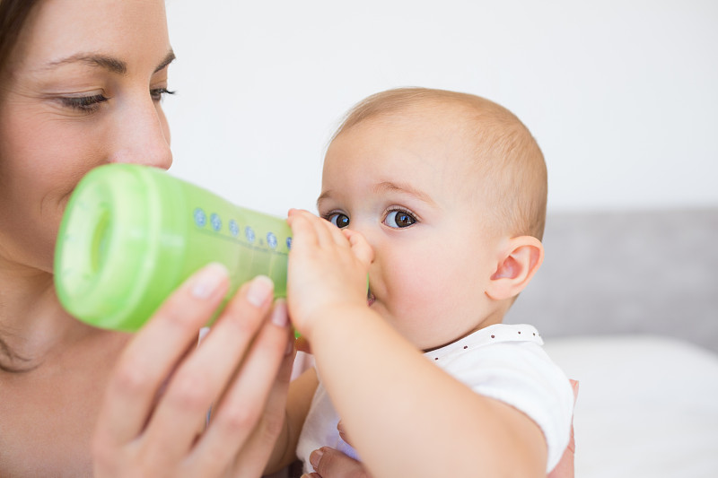 一个母亲在家里用奶瓶喂养婴儿的特写图片下载