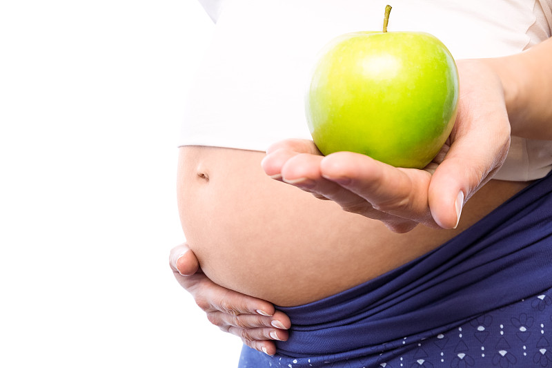 一名孕妇在白底上拿着绿苹果图片下载
