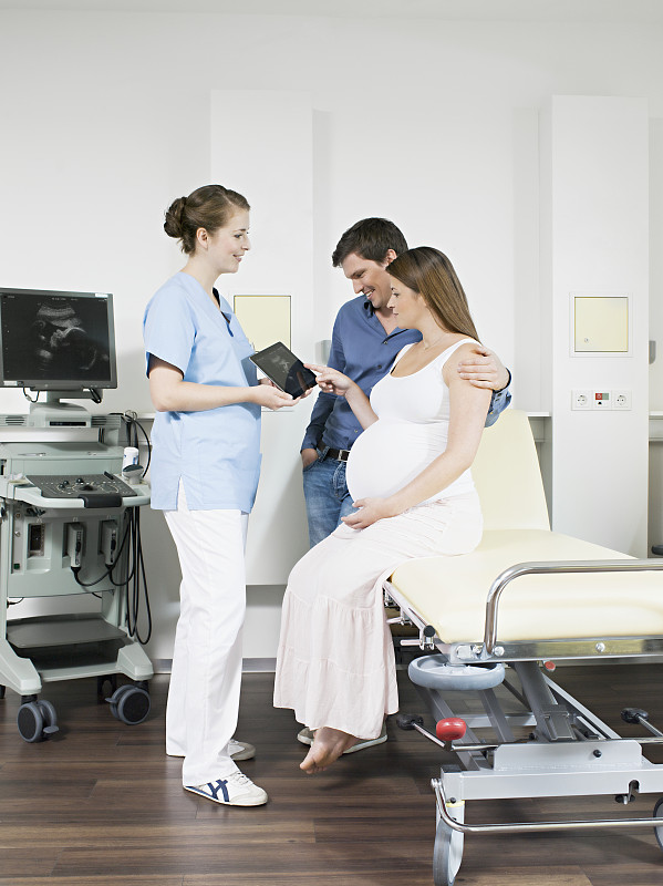 医生用平板电脑显示孕妇和丈夫的超声波扫描图图片下载