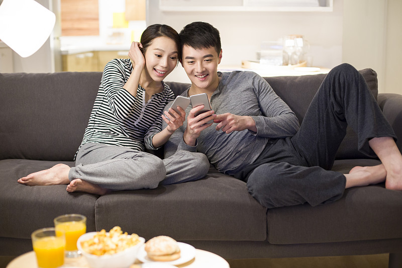 年轻情侣在客厅沙发上使用手机图片下载