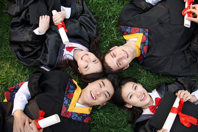 四个身穿学士服的大学生躺在草地上图片下载