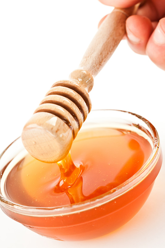 蜂蜜勺放在碗上，在白色的背景下滴下蜂蜜图片素材