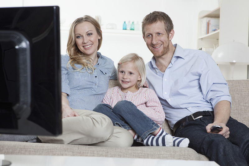德国，巴伐利亚，慕尼黑，一家人坐在沙发上看电视，面带微笑图片下载