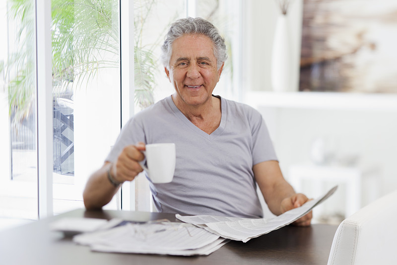 一个心情愉快的老人一边看报纸一边喝咖啡图片下载