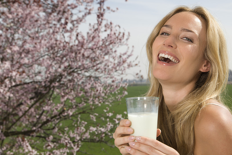 德国，北莱茵威斯特伐利亚，年轻女子拿着一杯牛奶，微笑着，肖像图片下载