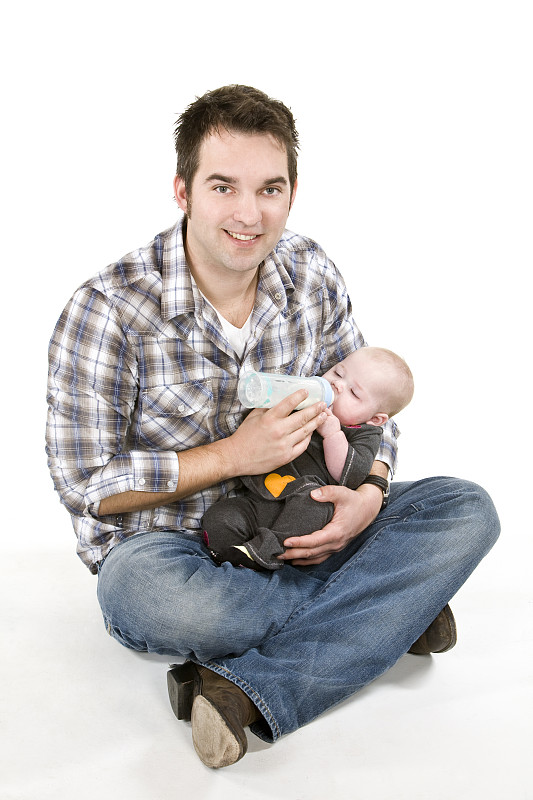 年轻的成年父亲正在给膝上的女婴喂奶图片素材