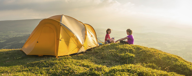 孩子们在夏季日落山顶彩色帐篷旁露营图片下载