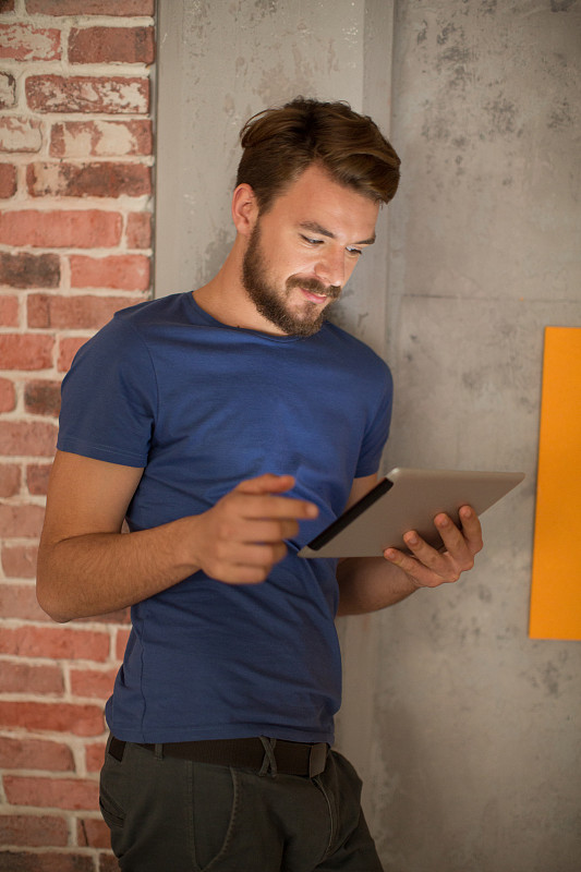 男人站在墙边，用着平板电脑。图片素材