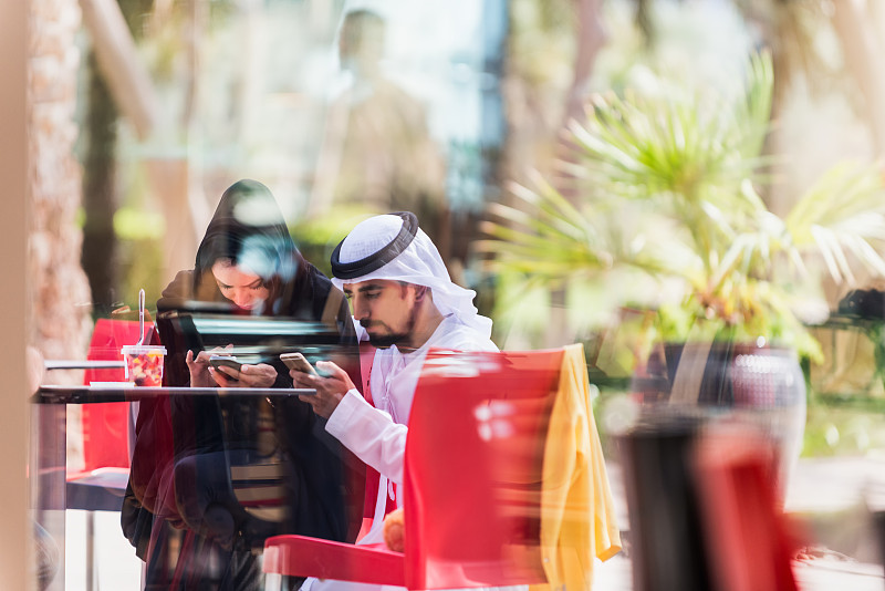穿着传统服装的中东夫妇在户外咖啡馆查看手机??图片下载
