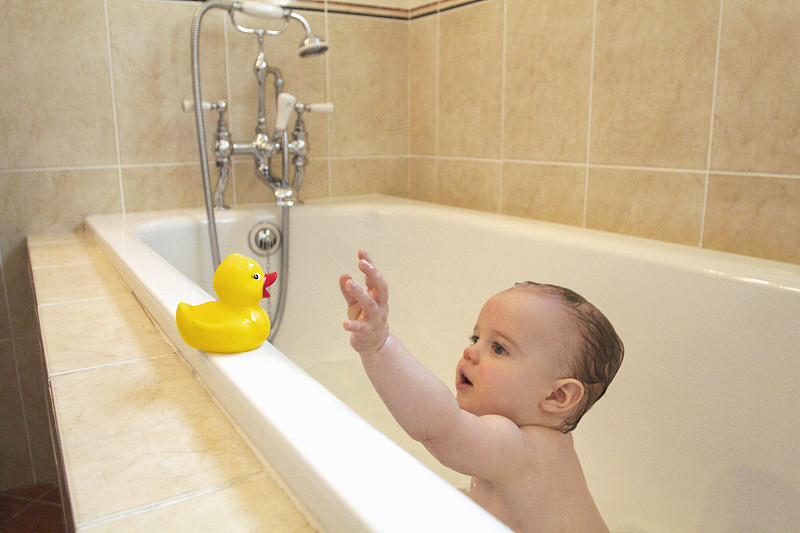 婴儿在洗澡，伸手去抓橡皮鸭图片下载