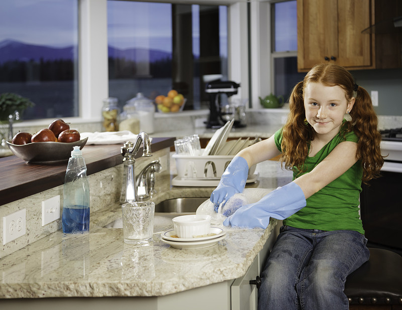 小红发女孩微笑着在晚上厨房洗盘子图片下载