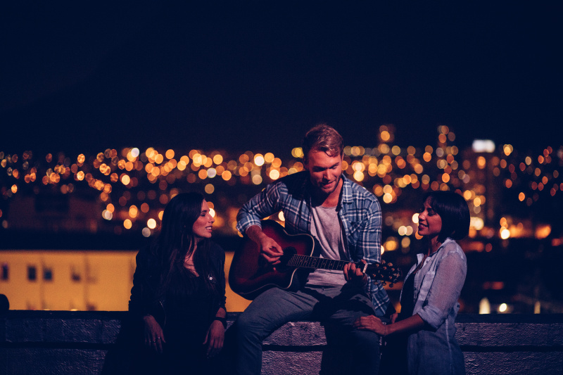 一个年轻人在屋顶上为他的两个朋友弹吉他图片下载