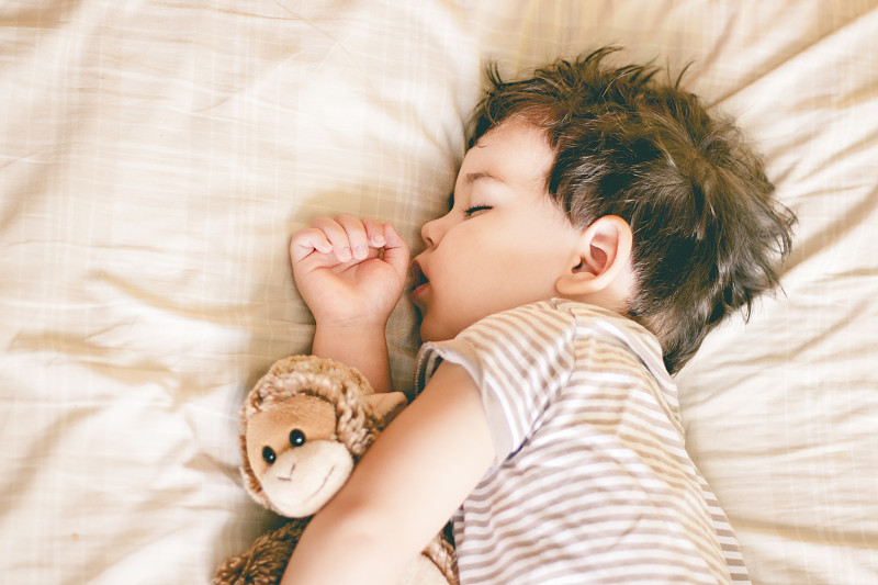 小男孩睡在床上，手里拿着一个柔软的玩具图片下载