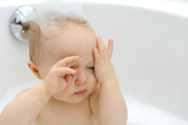 Baby girl in a bathtub wiping bath foam图片素材