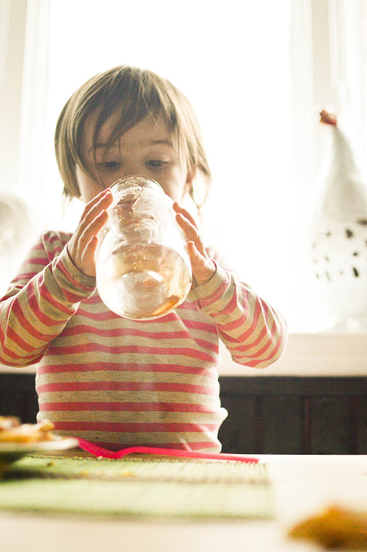 一个蹒跚学步的小女孩在看一个空糖浆罐。图片下载