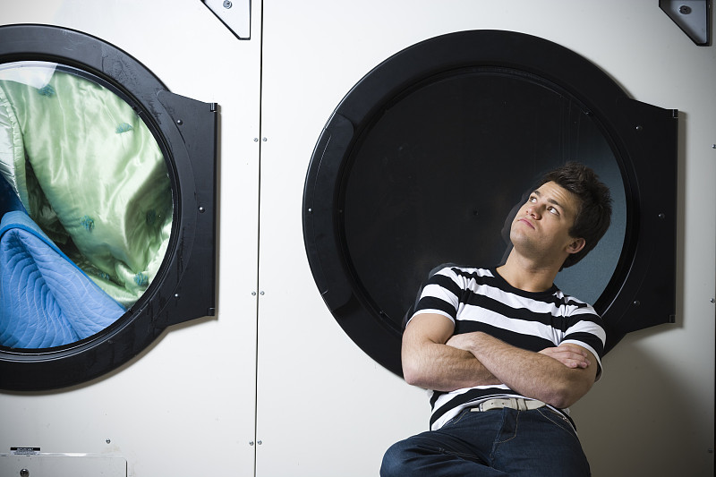 男人坐在洗衣店双臂交叉看着烘干机图片素材