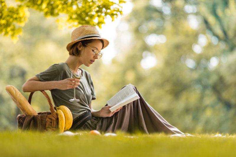 年轻女子放松与葡萄酒杯和阅读书籍在野餐。图片下载