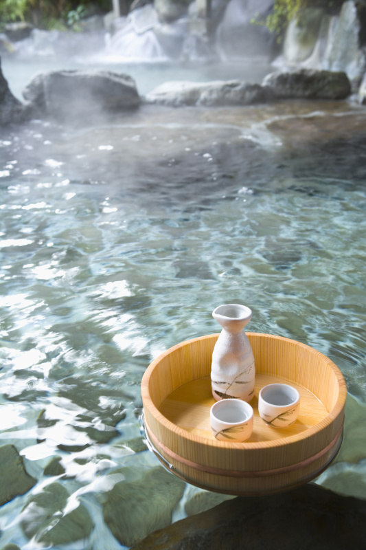 一个日本户外温泉浴，米酒瓶子和杯子在一个浮动的浴缸，高角度视图图片下载