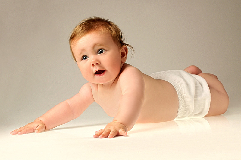 一个婴儿穿着尿布躺在她的腹部和推她的胳膊图片下载