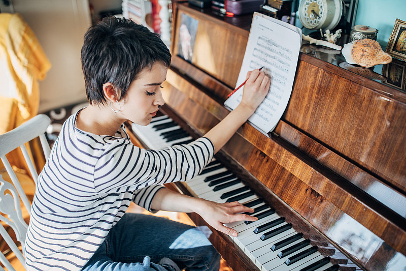 年轻的女钢琴家在自己家里的房间里谱曲图片下载