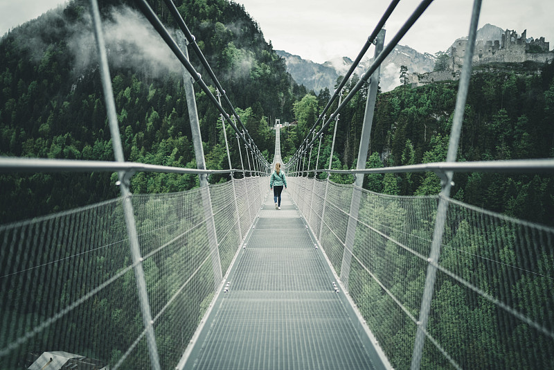 年轻女性徒步穿越高山环境中的吊桥图片下载