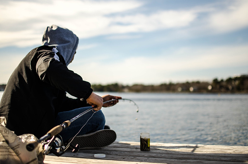 一名男子坐在湖边的码头上钓鱼图片素材