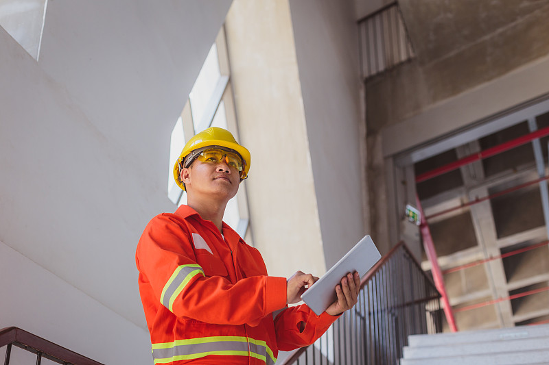 亚洲建筑或电子工程师戴安全帽穿安全夹克在建筑工地旁边用数码平板电脑，工程师在工地检查建筑项目图片下载