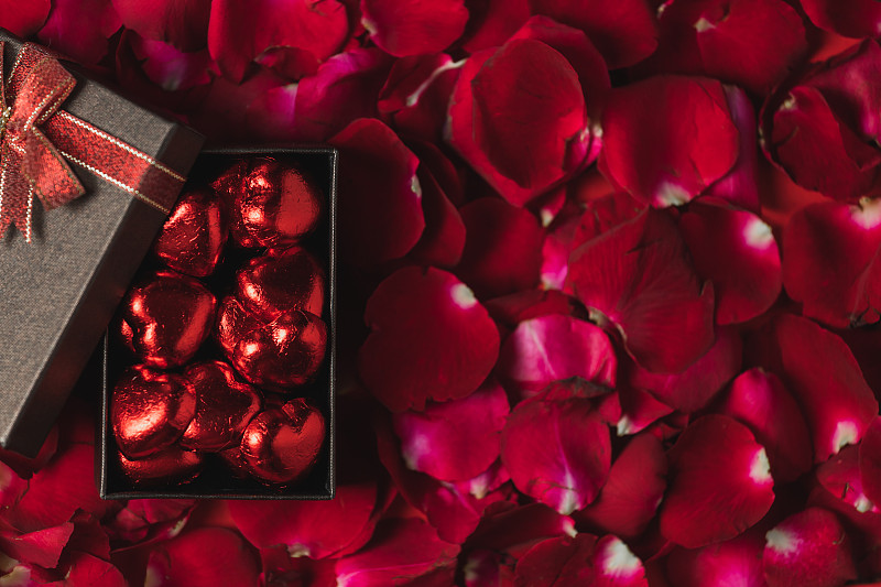 红色玫瑰花瓣上放置的棕色礼盒俯视图，情人节主题图片素材