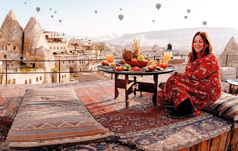 土耳其卡帕多西亚，日出时分，一名身穿红色衣服的妇女站在屋顶上图片下载