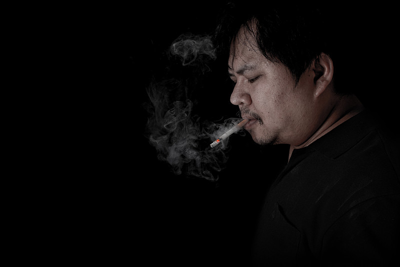 在黑色背景下抽烟的男人的肖像图片素材