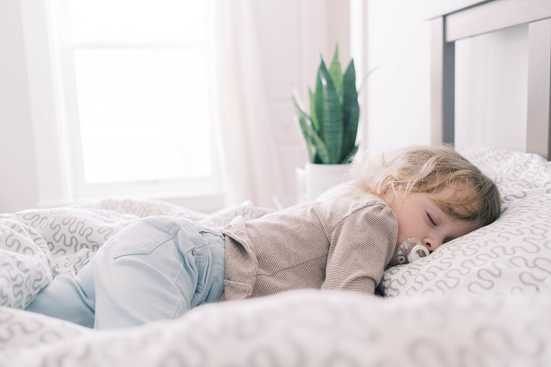 一个抱着奶嘴睡在父母床上的小孩。图片素材