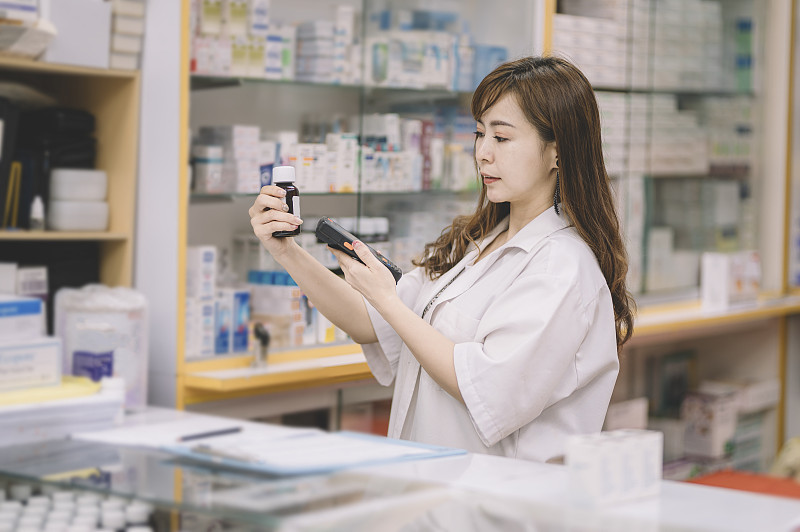 一位亚洲华裔女药剂师在收银台扫描一瓶药丸的价格信息图片下载