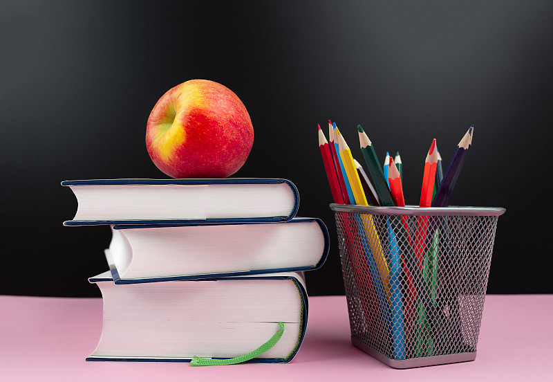 教育理念，新鲜苹果在一堆书旁边的铅笔杯和彩色铅笔图片素材