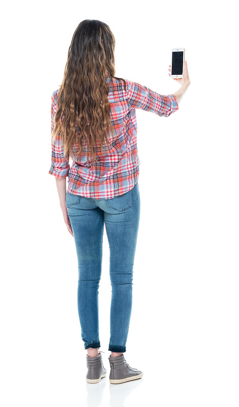 白人女性穿着牛仔裤站在白色背景前用手机拍照图片下载