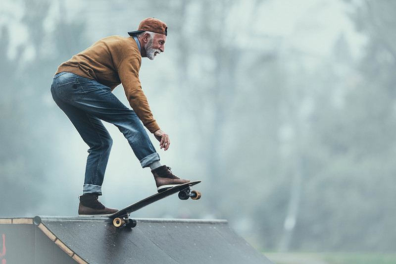 快乐的老人在公园的斜坡上玩滑板。图片素材