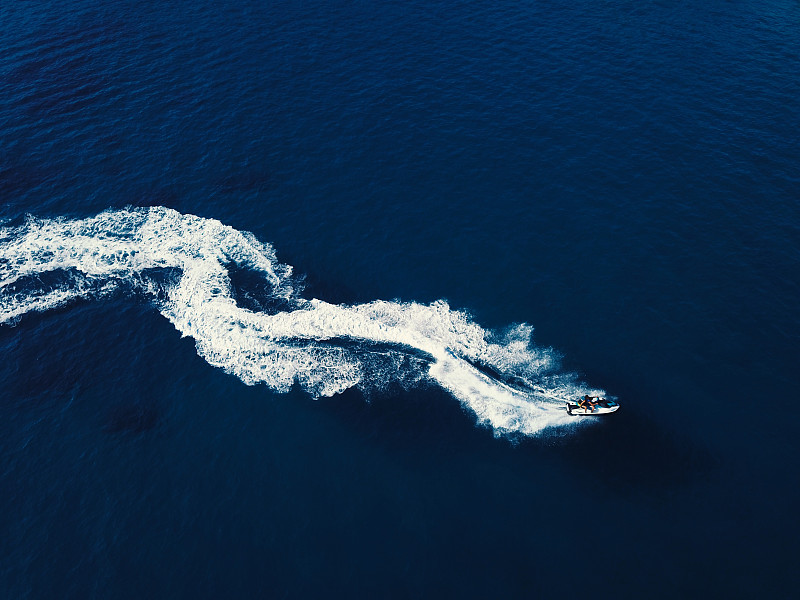 一艘喷气式快艇在深蓝色的海水中打旋的鸟瞰图。船的尾流从上面。图片素材