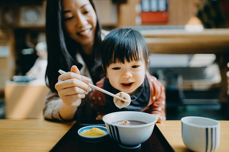 快乐的年轻亚洲母亲和可爱的小女儿分享日式甜点红豆汤和麻糬在传统风格的Kissaten咖啡馆餐厅图片素材