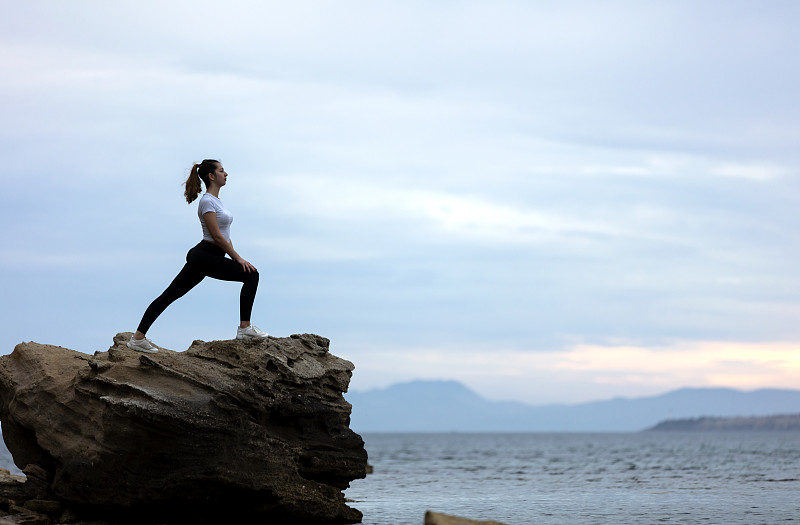 一个女人在海滩的岩石上做瑜伽图片下载