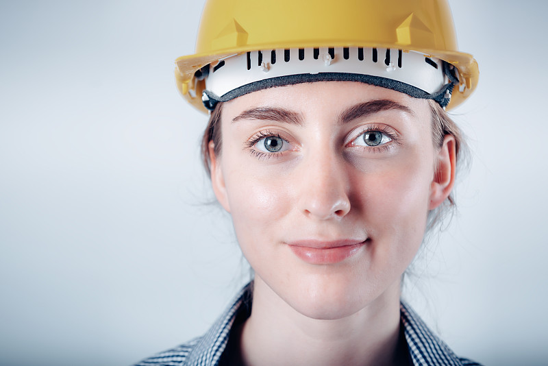 肖像的工程师妇女在安全帽安全设备站在孤立的背景，近距离拍摄的建筑工程师在保护工作服，而看着摄像机。工程职业和建筑行业摄影主题图片素材