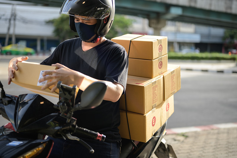 亚洲人戴着面具在摩托车上制造纸板箱图片下载
