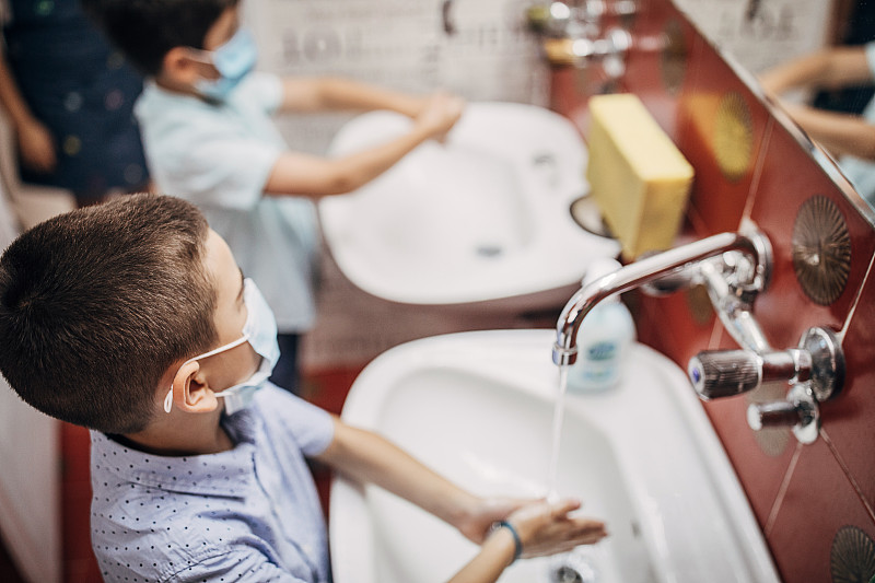 两个带着防护口罩的小男孩在进入教室前用肥皂洗手图片素材