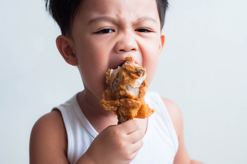 一个东南亚男孩正在吃炸鸡，背景是白色的图片素材