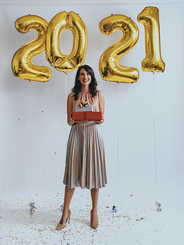 新的2021快乐!一个快乐的女人站在新年的气球下拿着礼物(看着相机)图片下载