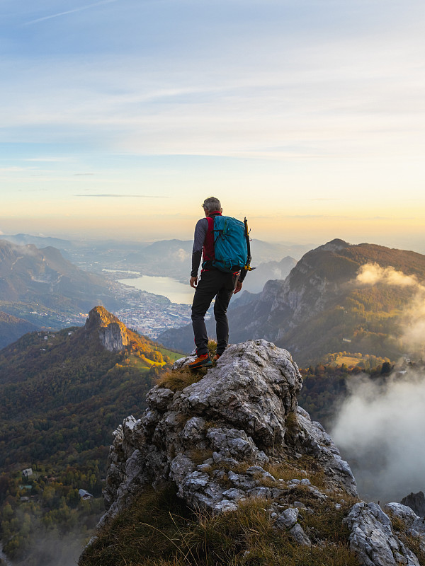 沉思的徒步旅行者背着背包站在山顶在日出的贝加马斯克阿尔卑斯山，意大利图片素材