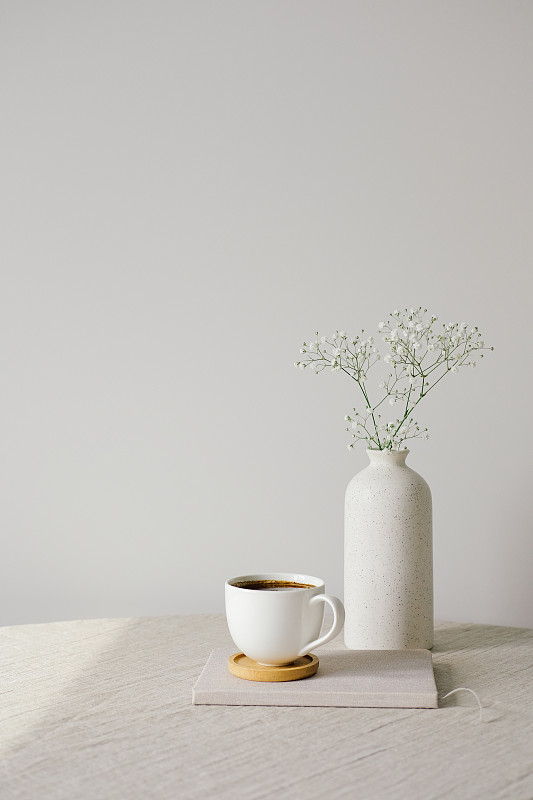 斯堪的纳维亚、北欧风格的家居室内装饰。桌上放着一杯咖啡和一瓶花，亚麻桌布上。背景是白色的墙。早上,早餐概念图片下载